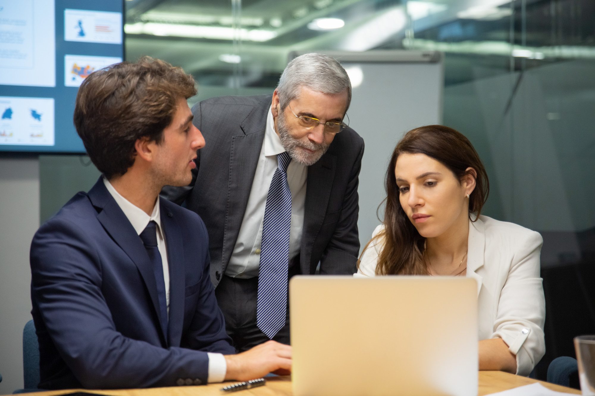 Three professionals in business attire collaborating on a laptop during a conference room meeting